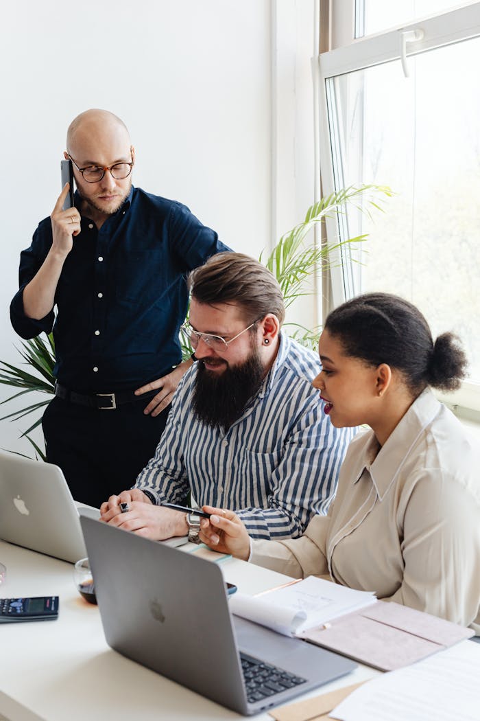 A diverse group of professionals engaged in a collaborative team meeting at a modern office with laptops and mobile phones.